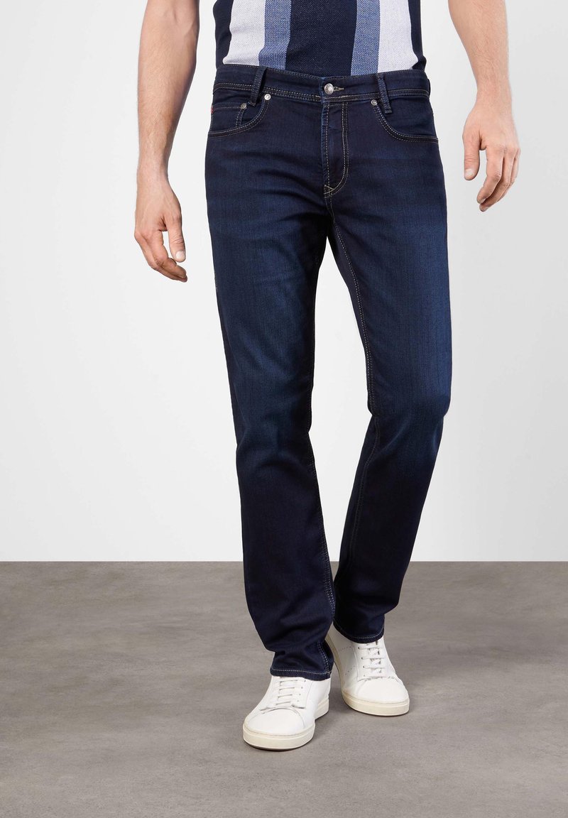 Dunkelblaue Jeans aus Denim mit geradem Schnitt, ausgestattet mit klassischem Fünf-Taschen-Stil und dezenten Kontrastnähten, kombiniert mit weißen Sneakers.