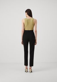 Gullstripet, ermeløs topp parret med tettsittende svarte bukser og lyse hæler. Outfiten har et minimalistisk design og glatte teksturer.