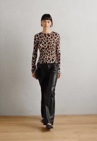 Langermet topp i leopardmønstret stoff, kombinert med tettsittende svarte lærbukser. Modellen holder en svart clutch og har kort hår.