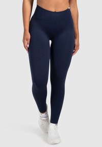 Marina högmidjade leggings tillverkade av elastisk tyg, med en slät yta och en figurnära design, parat med vita träningsskor.