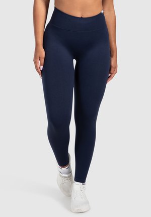Marineblauwe high-waisted leggings van rekbaar materiaal, met een fijne textuur en een aansluitend ontwerp, gecombineerd met witte sportschoenen.