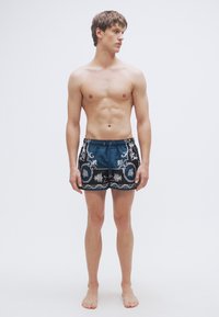 Ανδρικό μαγιό βερμούδα σε μπλε χρώμα με περίπλοκα γκρι λουλουδάτα σχέδια. Κατασκευασμένο από απαλό ύφασμα, διαθέτει ελαστική μέση και κορδόνι ρύθμισης.