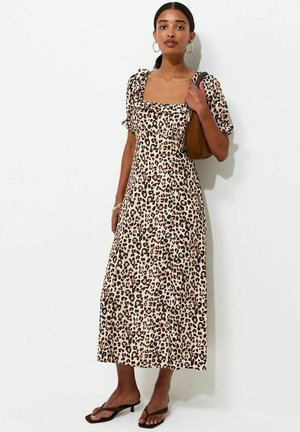 Femme portant une robe midi à imprimé léopard avec des manches bouffantes, portant un sac à bandoulière marron et des sandales noires à talons.