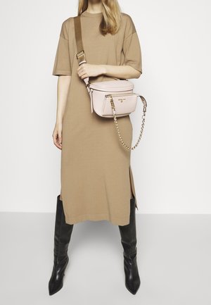 Vestido midi marrón de punto con aberturas laterales, combinado con un pequeño bolso cruzado rosa con cadena y detalles en dorado, y botas negras hasta la rodilla.