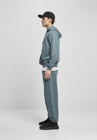 Felpa blu chiaro con cappuccio, pantaloni sportivi coordinati e scarpe da ginnastica nere. L'outfit presenta una vestibilità rilassata e una trama del tessuto liscia.