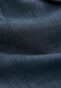 Tmavě modrá džínovina s viditelným prošíváním a jemnou strukturou, ukazující přirozené záhyby a stíny.