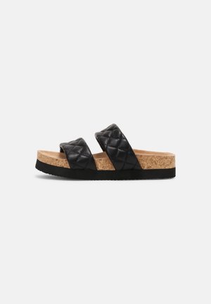 Sort quiltet sandal med dobbelte stropper, kork-fodbed og sort sål, vist fra siden på en ensfarvet hvid baggrund.