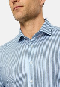 Hemd mit Knopfleiste in Blau und Weiß mit vertikalen Streifen, einem spitzen Kragen und einer strukturierten Passform. Hergestellt aus einem leichten Stoff.