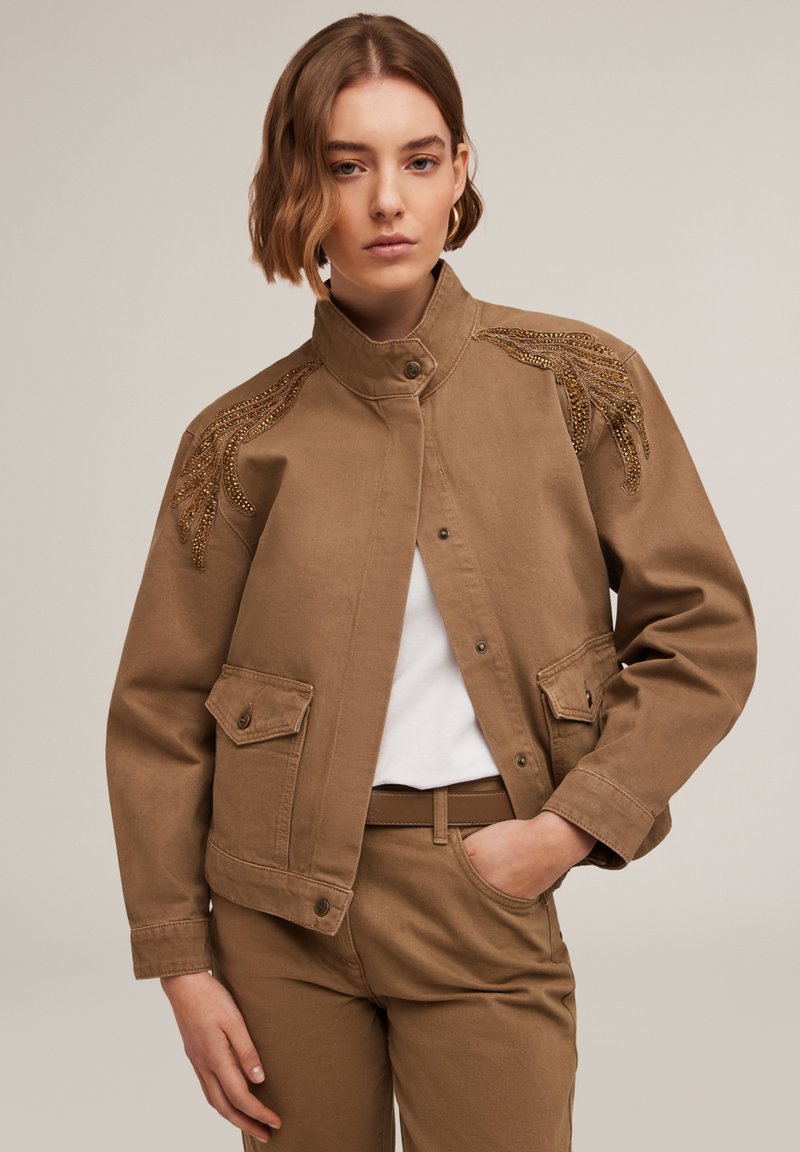 Veste en denim brun avec un col structuré, fermeture à boutons et détails embellis sur les épaules. Deux poches avant, tissu texturé.