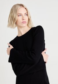 Black long-sleeve top with a round neckline and bell-shaped cuffs. Made from a soft fabric, features a subtle texture and clean lines.
