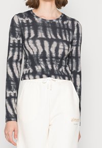 Maglia aderente a maniche lunghe di colore grigio scuro con motivo in tie-dye chiaro; tessuto morbido; scollatura rotonda; indossata con pantaloni della tuta chiari.