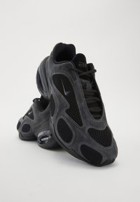 Des chaussures de sport noires alliant une combinaison de matériaux en suède et en maille, un design arrondi, des semelles texturées et des découpes distinctes pour la ventilation.
