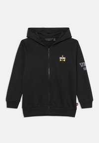 Čierna mikina na zips z bavlnenej zmesi, s žltým logom "Ninjago" na hrudi a šedým textom na rukáve. Klokaní vrecko vpredu.