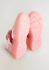 Baskets pour enfants roses avec une bande Velcro, présentant un matériau lisse, des motifs en forme de cœur et des semelles en caoutchouc texturé.