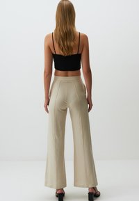 Pantalons beige à jambe large en tissu doux, dotés d'une taille haute et de lignes épurées, assortis d'un crop top noir ajusté.