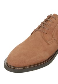 Braune Wildleder-Schnürschuhe mit runder Spitze, kontrastierenden Nähten und einer dunklen Gummisohle. Verfügt über eine glatte, matte Textur.