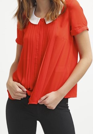 Rode, doorschijnende blouse met korte mouwen en een witte kraag. Heeft plooien aan de voorkant en een losse pasvorm, gecombineerd met donkere broek.