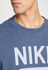 Blå bomulds t-shirt med rund hals og hvidt Nike-logo. Stoffet ser blødt ud med en glat tekstur og minimal syning.