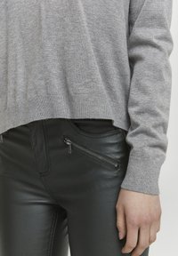 Grå strikket trøje med en cropped design, parret med sorte faux læder bukser med lynlåslommer på siden. Glat tekstur overalt.