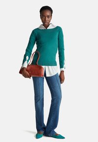 Zelený pletený svetr s lodičkovým výstřihem, přes bílou košilovou halenu. Rozšiřující se modré džíny a hnědá kožená kabelka. Špičaté tyrkysové baleríny.