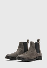 Botas Chelsea de ante gris con paneles laterales elásticos, suela de goma plana y una lengüeta en la parte trasera para ponérselas fácilmente. Diseño y textura sencillos.