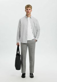 Camicia a maniche lunghe a righe in azzurro chiaro e bianco, abbinata a pantaloni grigi su misura. Una borsa nera e scarpe completano l'outfit.