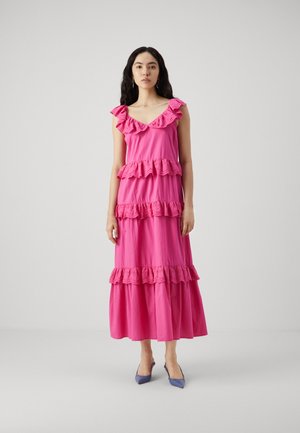 Pink maxi dress with ruffle detailing on neckline and tiers, cotton material, relaxed fit, paired with blue pointed-toe heels.