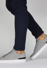 Zapatillas de ante gris con suela blanca y acento negro en el talón, combinadas con pantalones azul marino, que muestran un diseño estilizado y un ajuste casual.