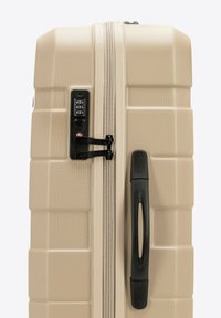Valigia rigida beige, con superficie testurizzata, cerniera e lucchetto neri, e manico retrattile per facilitare il trasporto.