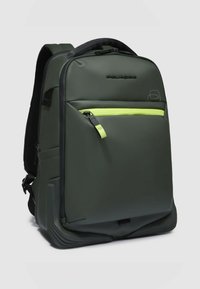 Mochila impermeable verde con una textura suave, que presenta un bolsillo frontal con cremallera en verde neón y correas ajustables para los hombros.