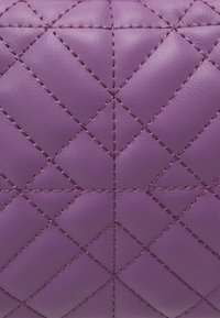 Pelle in ecopelle viola trapuntata con motivo a rombi e dettagli di cucitura a contrasto. Texture liscia con una finitura lucida.