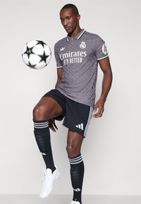 Maglia da calcio grigia con un motivo sottile, pantaloni corti neri e calze nere con strisce bianche. Palla da calcio bianca con stelle nere.