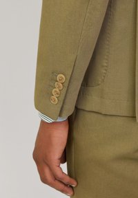 Olivgrön kostymjacka med ärm som har fem beige knappar, kontrasterande randig tyg som syns från manschetten, strukturerat material.