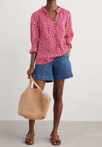 Rød blomsterbluse med lange ærmer, parret med blå denim shorts. En tan vævet totebag og brune sandaler fuldender looket.
