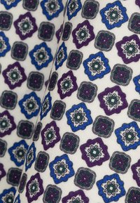 Tkanko z powtarzającym się geometrycznym wzorem kwiatowym w odcieniach niebieskiego, fioletowego i zielonego na jasnobeżowym tle. Wzór ma teksturowane wykończenie.