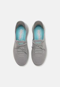 Baskets grises en maille à enfiler avec une surface texturée, des lacets élastiques et une semelle intérieure bleu clair portant la marque "SKECHERS Slip-Ins".