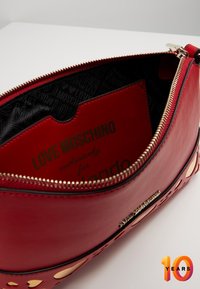 Pochette en simili cuir rouge avec accents dorés, fermeture zippée et intérieur noir à motif avec le détail du logo "LOVE MOSCHINO".