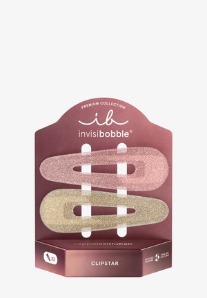 To glitrende hårklemmer, en lyserød og en gylden, vist på en mauve emballage mærket "invisibobble CLIPSTAR" med genbrugssymboler.