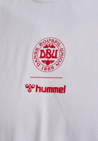 Biały materiał z czerwonym, okrągłym logo Dansk Boldspil-Union 1889 nad czerwoną nazwą marki hummel i logo pszczoły.