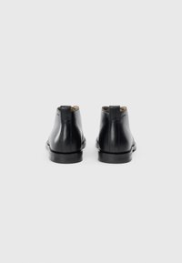 Botine negre din piele cu o textură netedă, vârf rotund și toc mic. Prezintă o bandă pentru tragere la spate, pentru a fi ușor de încălțat.