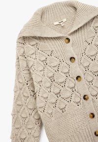 Beżowy sweter z dzianiny z żeberkowym kołnierzem, z teksturowanym wzorem w romby i drewnianymi guzikami z przodu.