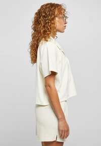 Helles beiges zweiteiliges Outfit aus weichem, strukturiertem Stoff, bestehend aus einem kurzärmligen Crop-Top und passenden Shorts mit seitlichen Schlitzen.