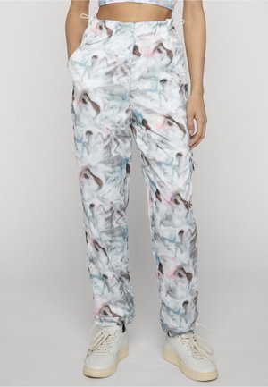 Kvinde iført bukser med abstrakt print i hvid, lyseblå og pink med snøre i talje og ankler, kombineret med hvide sneakers.