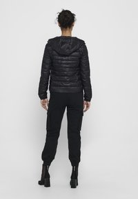 Black puffer jacket with a hood, featuring a quilted design and ribbed cuffs, paired with black cargo pants and high-heeled ankle boots.