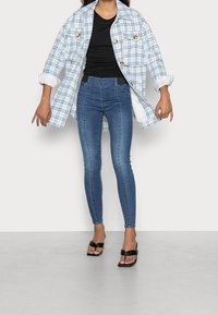 Chaqueta de cuadros azul y blanca con dos bolsillos en el pecho, camiseta negra ajustada y jeans skinny azules. Sandalias planas negras completan el conjunto.
