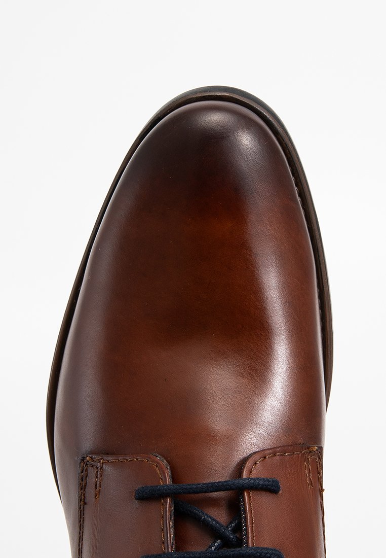 Braune Lederschuhe mit einem polierten Finish, runder Spitze und marineblauen Schnürsenkeln. Verfügt über gestickte Details und eine subtile Naht entlang der Oberseite.