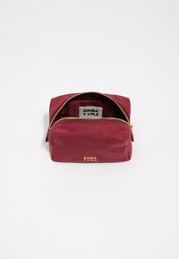 Neceser burdeos hecho de material suave con un zipper dorado y detalle de logo. Presenta una forma rectangular y una apertura en la parte superior.