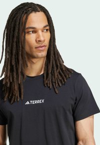 Camiseta negra de algodón con mangas cortas, que presenta un logo blanco "TERREX" en el pecho y un clásico escote de cuello redondo.
