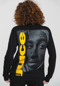 Black long-sleeve shirt featuring a large gray graphic face print with the word "Juice" in bold yellow letters vertically along the back.
