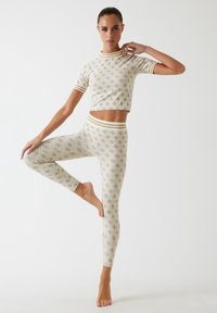 Dwuczęściowy zestaw odzieży sportowej wykonany z lekkiego materiału; krótki top z krótkim rękawem oraz dopasowane legginsy w kolorze kremowym z brązowymi geometrycznymi wzorami i paskami.